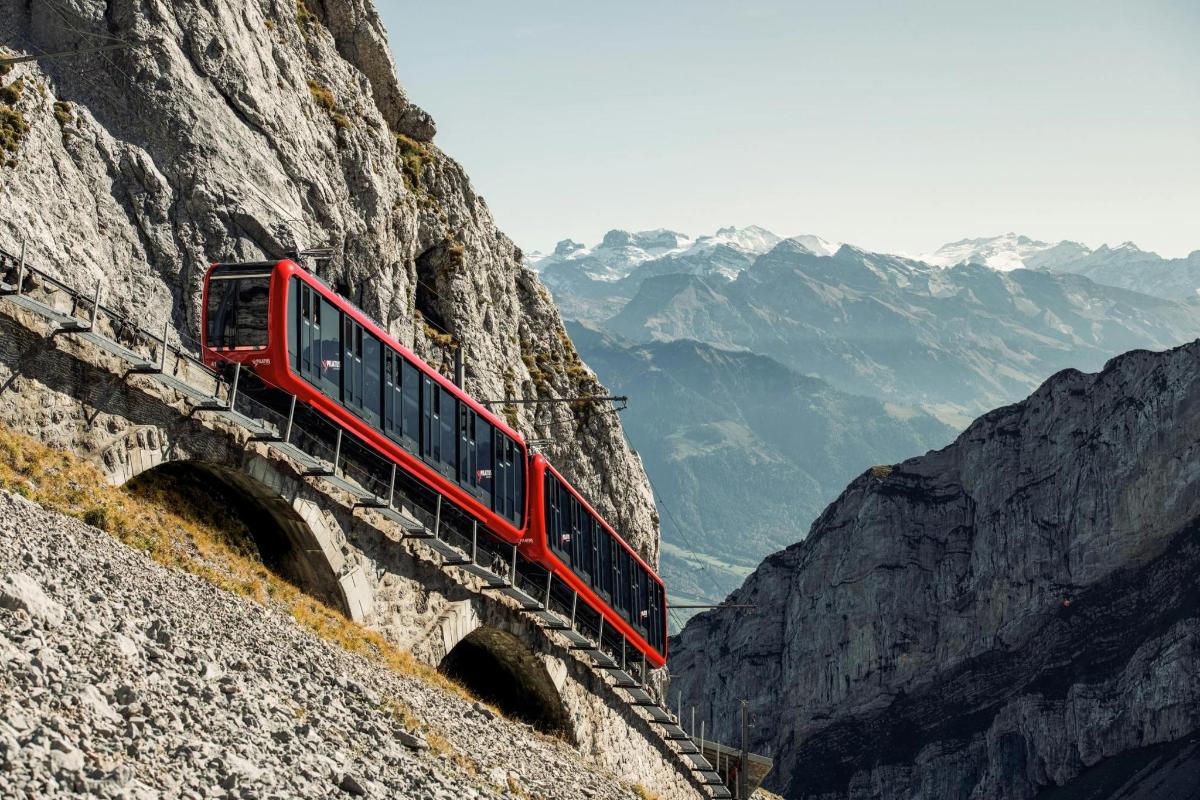 um trem vermelho está passando por um penhasco na montanha