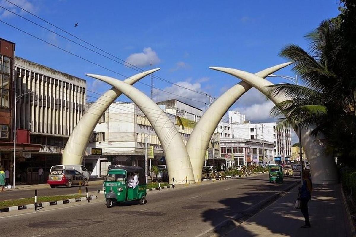 un'auto verde che percorre una strada cittadina con una scultura