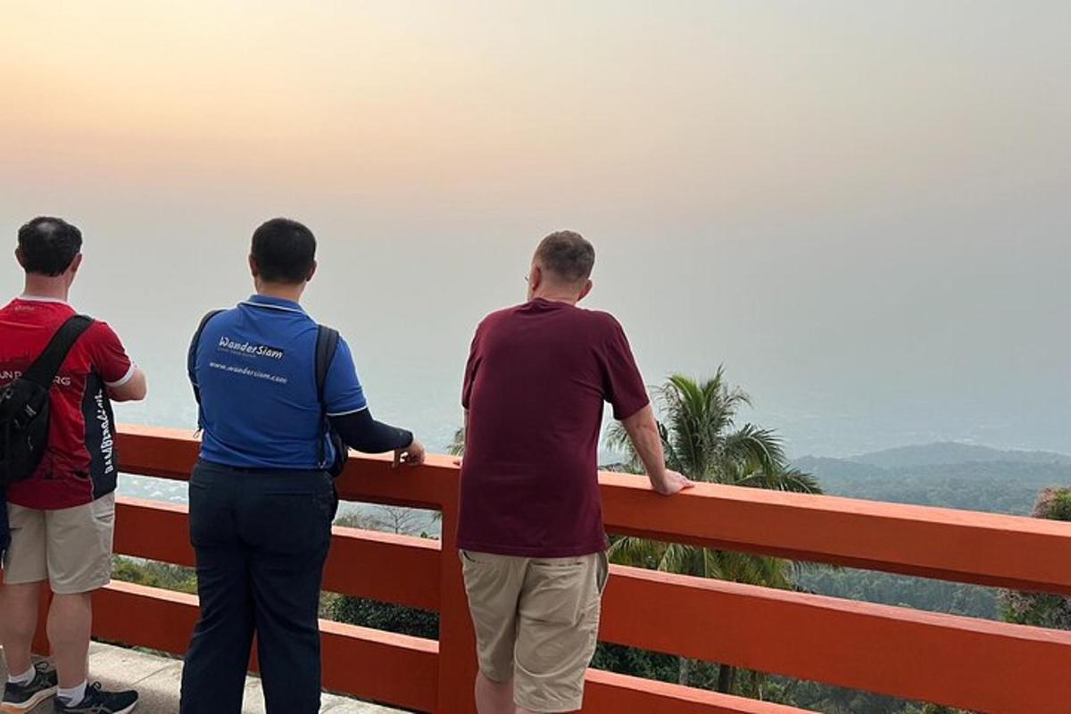 drie mannen staan op een hek en kijken uit over de oceaan