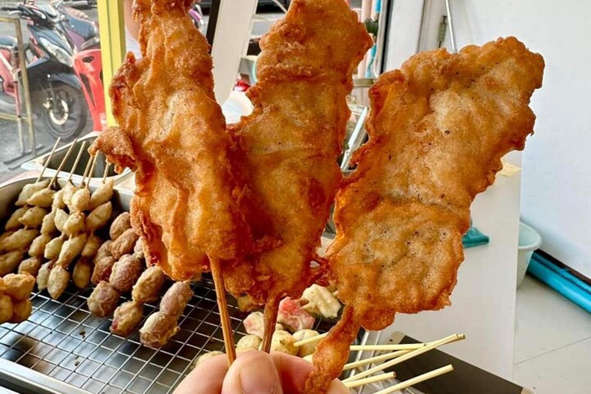 a person holding up three pieces of fried chicken on skewers