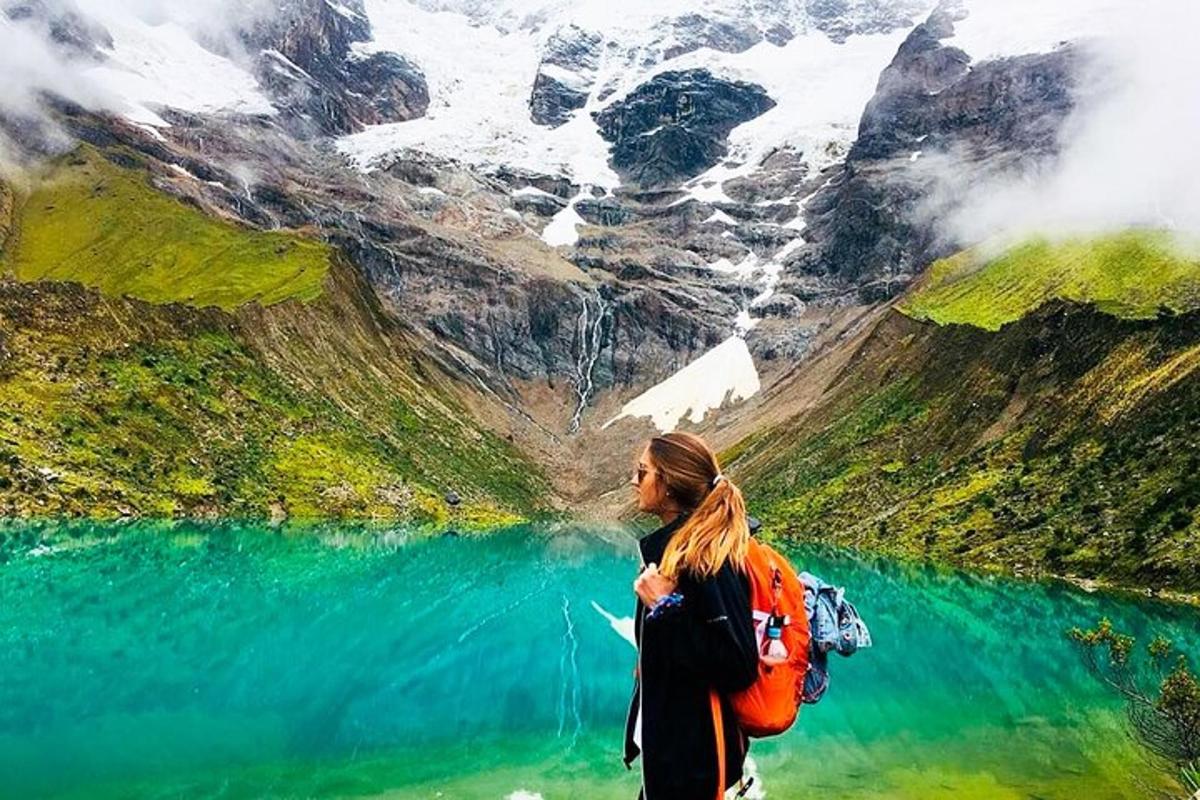 Una mujer con una mochila de pie cerca de un lago de montaña