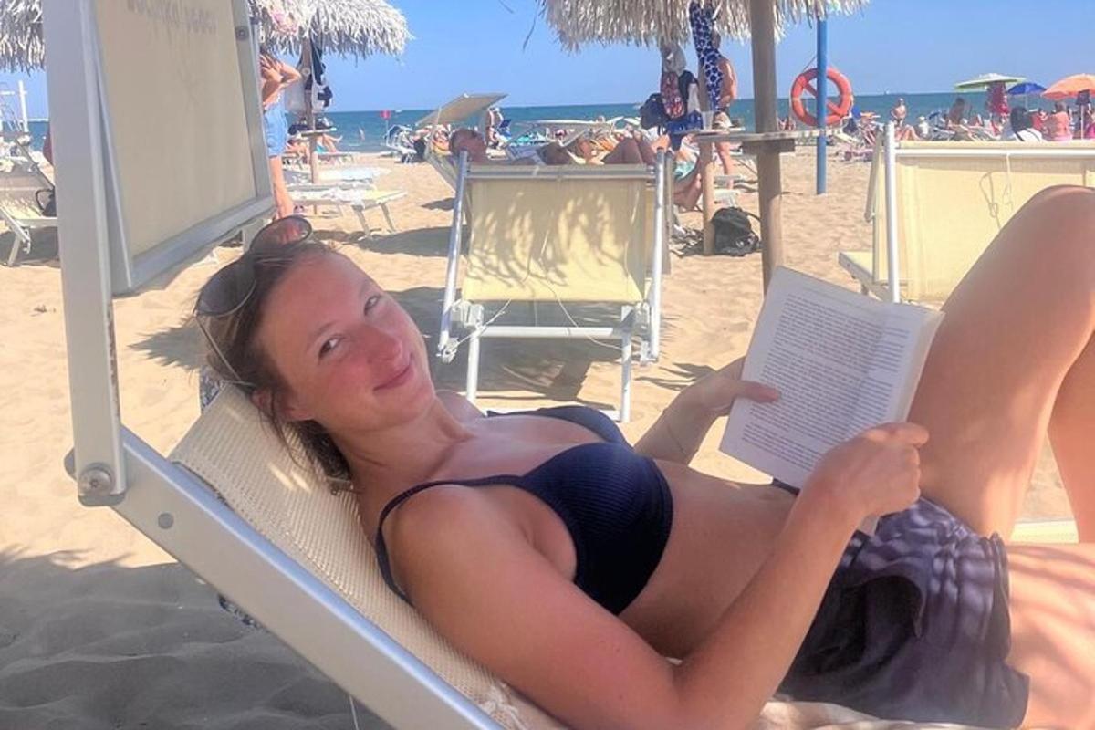 una dona estirada a la platja llegint un llibre