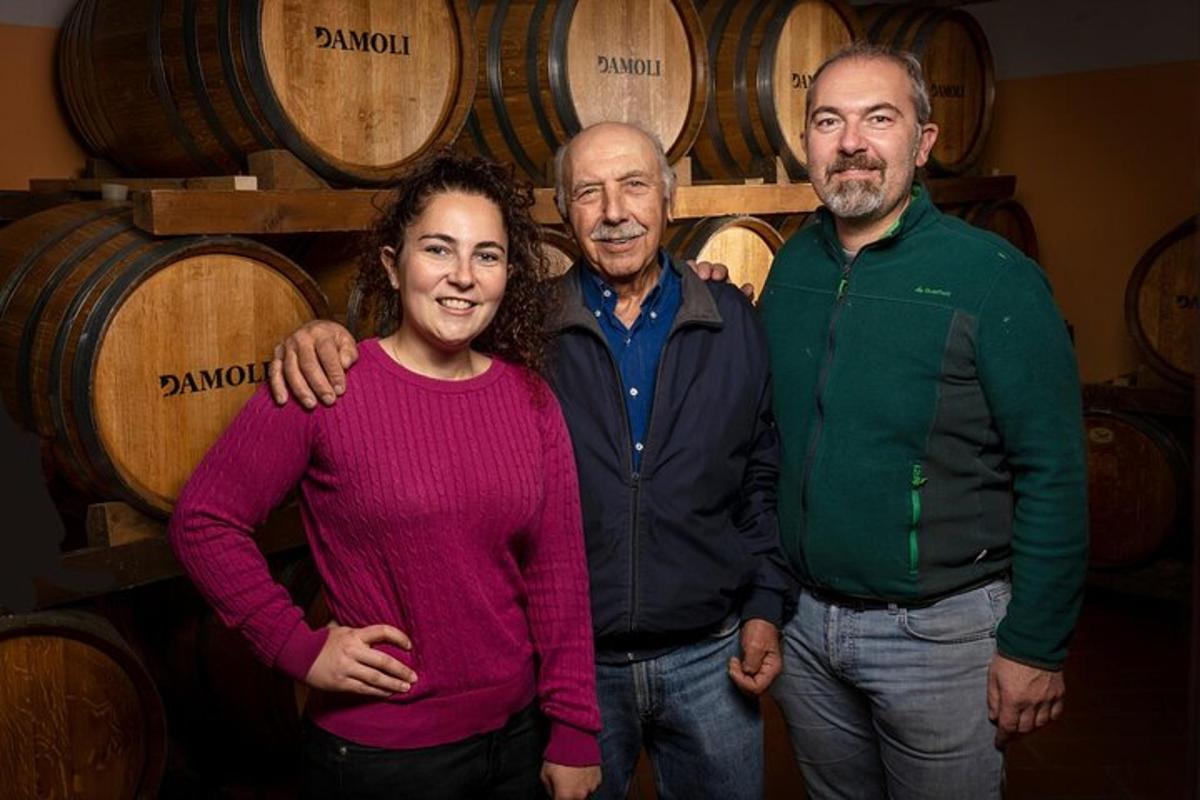 três pessoas em pé na frente de um monte de barris de vinho