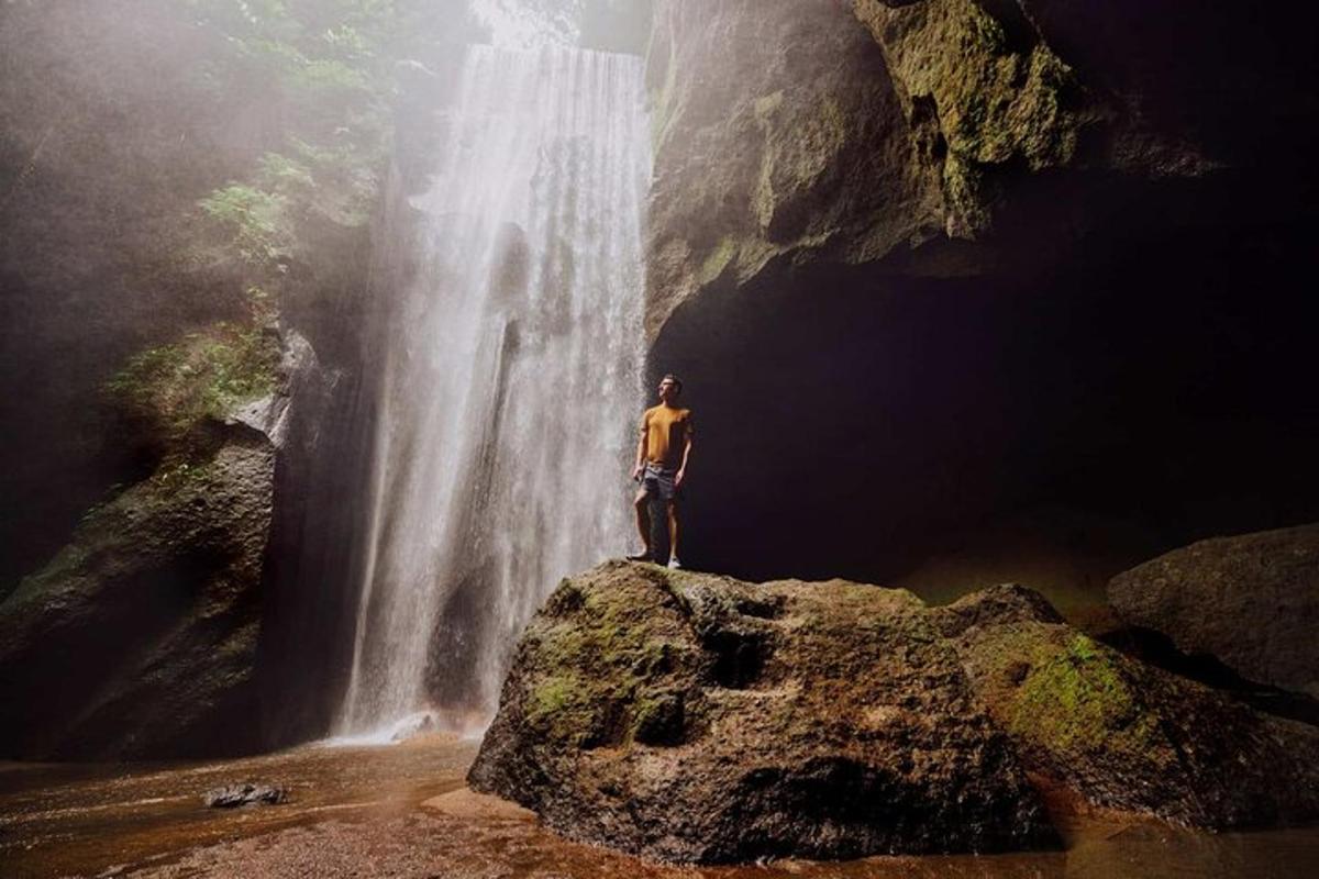 seorang lelaki berdiri di atas batu di hadapan air terjun