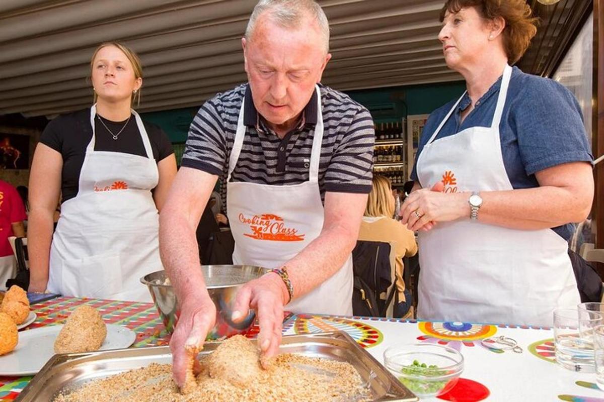 Un hombre preparando comida en una cocina con dos mujeres.