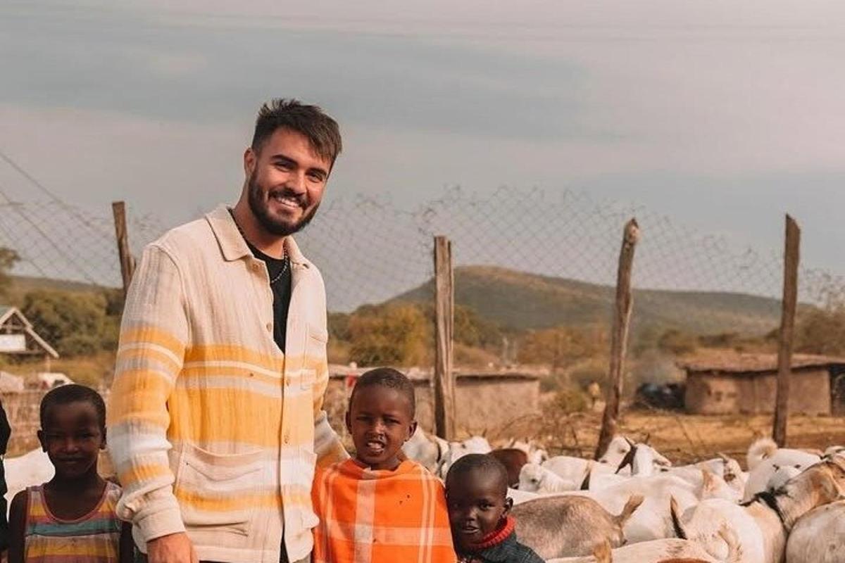 Un hombre de pie con dos niños frente a un rebaño de ovejas
