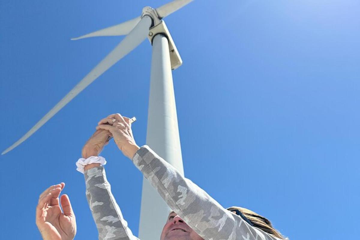 moški in ženska, ki držita roke dvignjene pred vetrno turbino