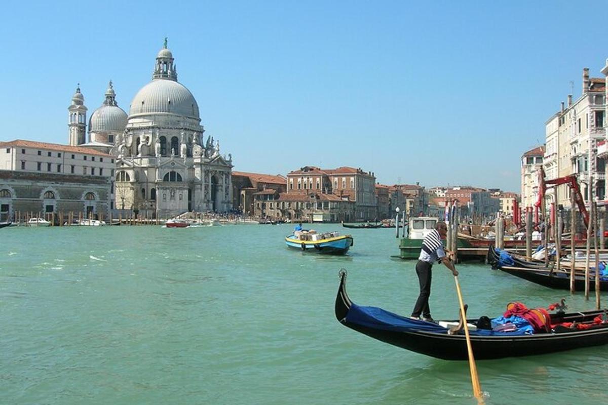 seorang lelaki sedang mendayung gondola di dalam air berhampiran sebuah bandar