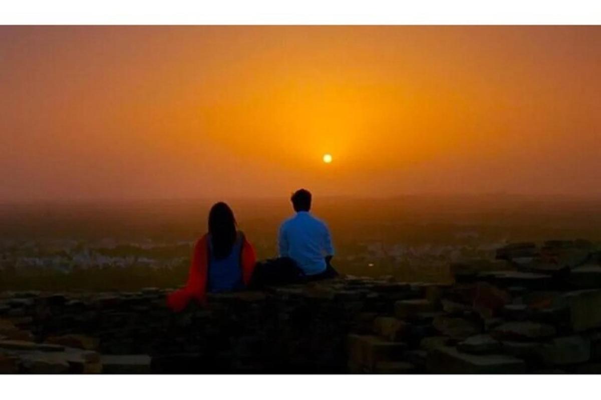 een man en een vrouw zitten op een rots en kijken naar de zonsondergang