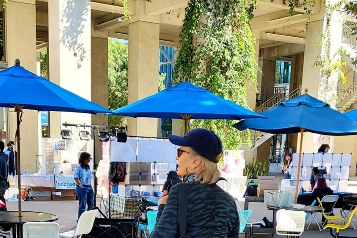 a woman sitting at a table under blue umbrellas