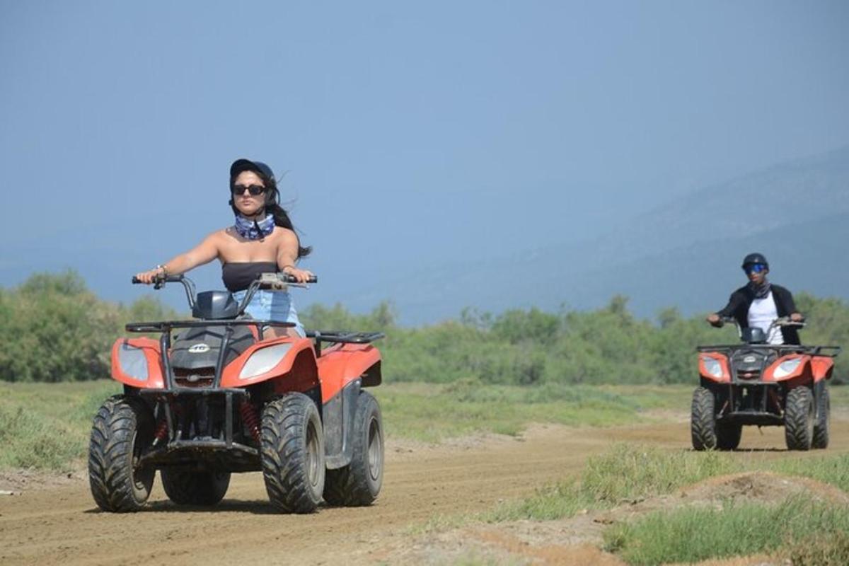two people riding on atvs on a dirt road