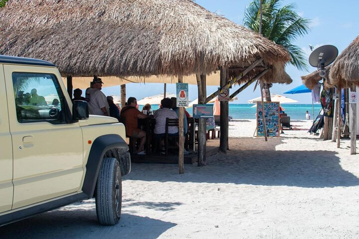 un camion parcheggiato su una spiaggia con persone sedute sotto un ombrellone di paglia