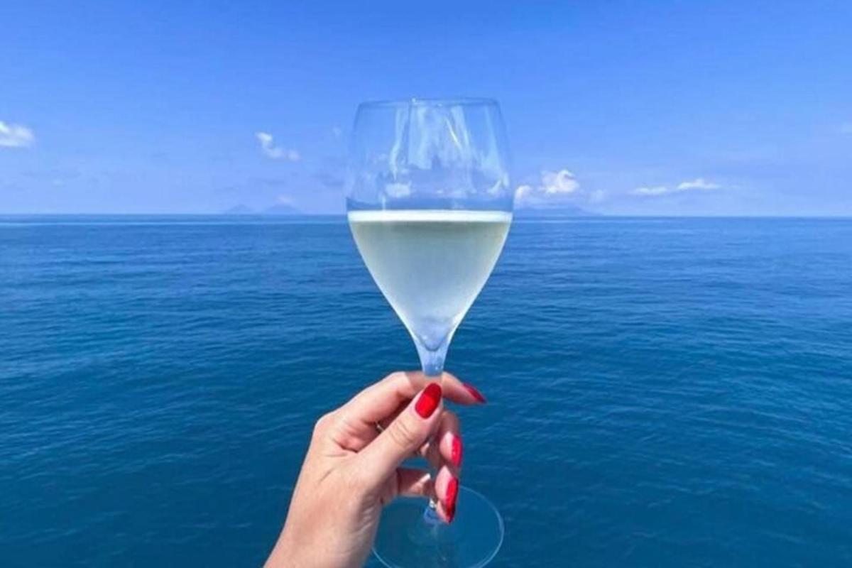 a hand holding a glass of white wine over the ocean