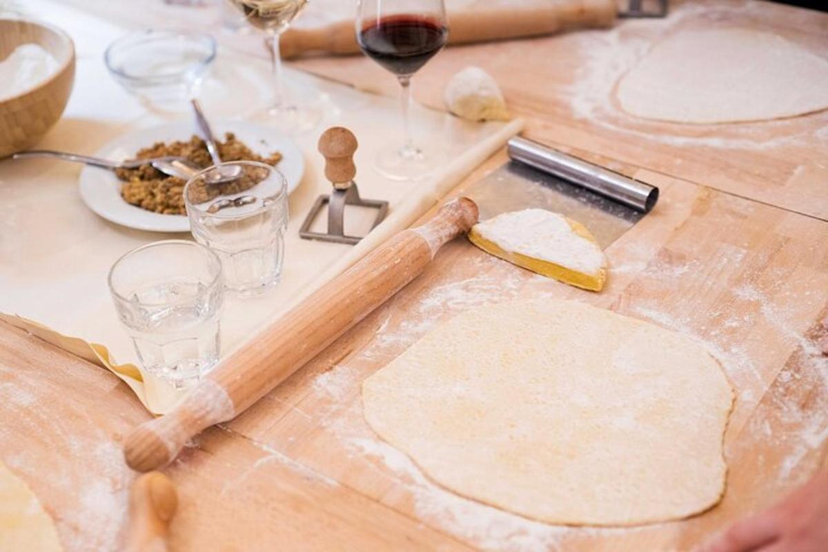 Una mesa con una tabla de cortar con masa y copas de vino.