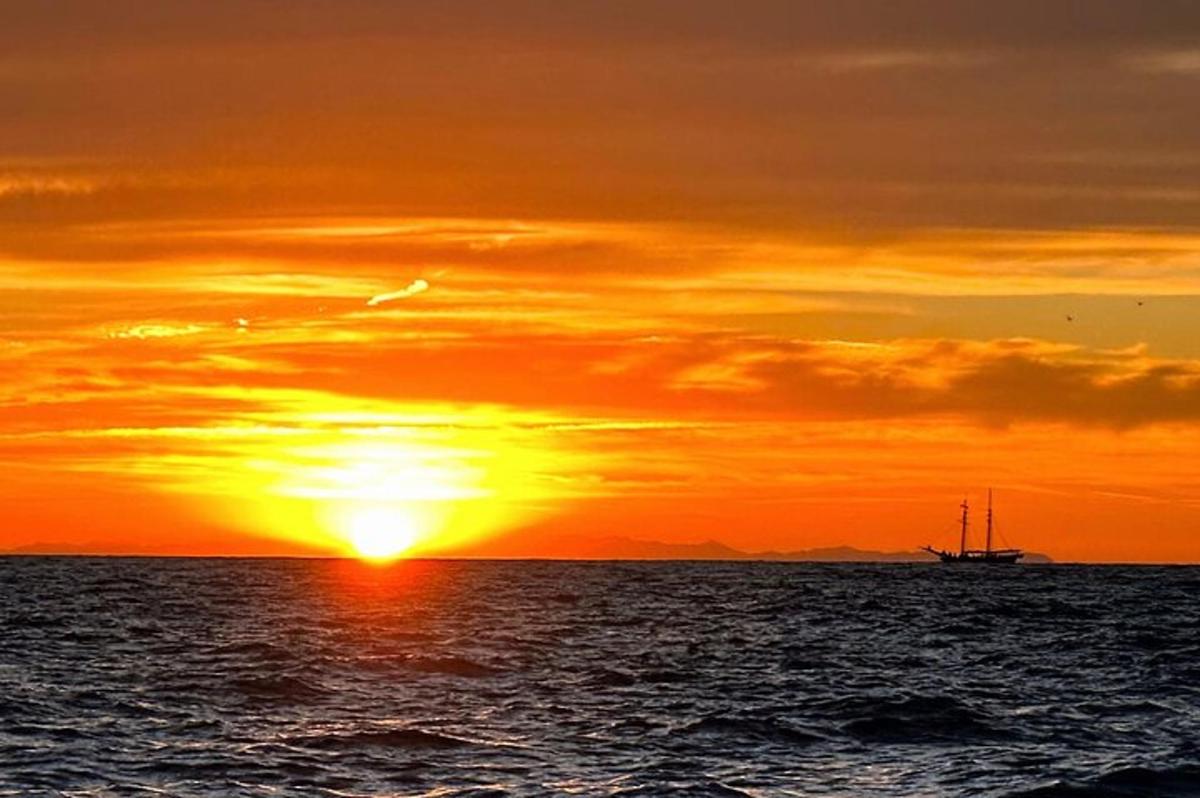um pôr do sol sobre o oceano com um barco na água
