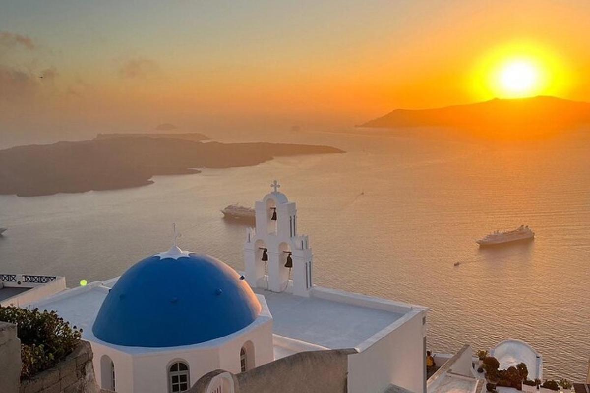 Una iglesia con una cúpula azul y una puesta de sol sobre el agua.