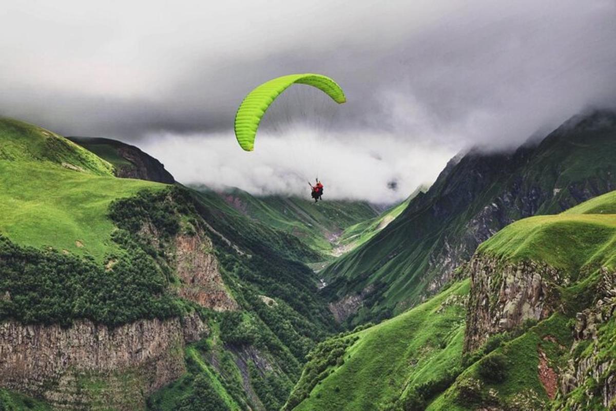 eine Person, die mit einem grünen Fallschirm über einen Berg reitet