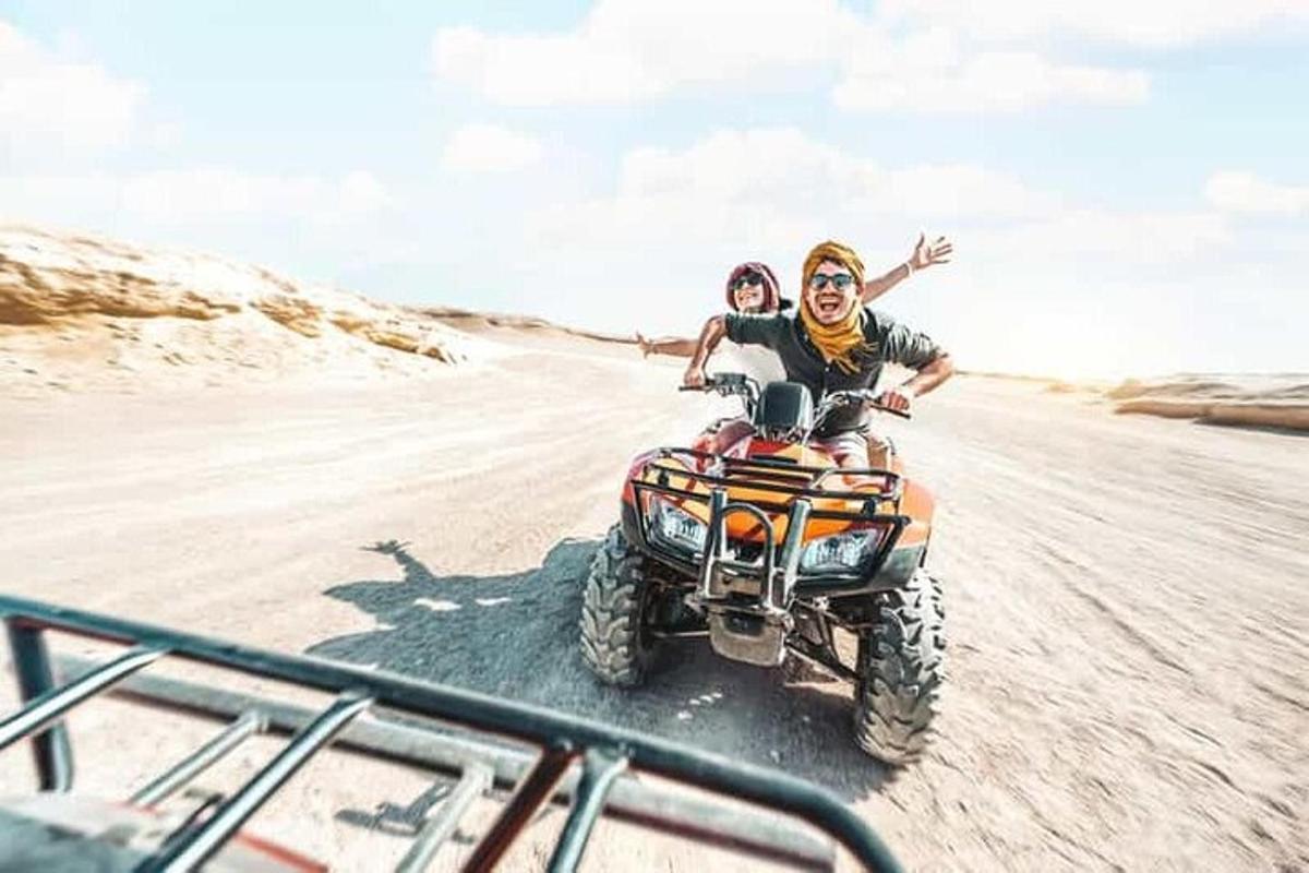 Un hombre y una mujer viajando en un vehículo de cuatro ruedas por el desierto.