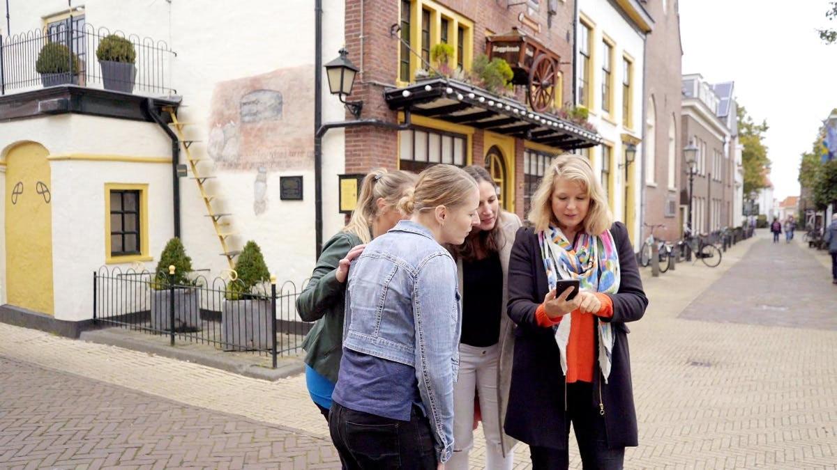 Tres chicas paradas en una calle mirando un teléfono celular