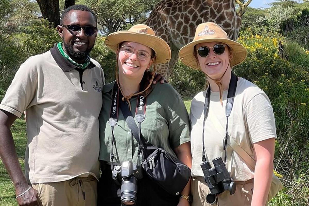un grup de tres persones dretes davant d'una girafa