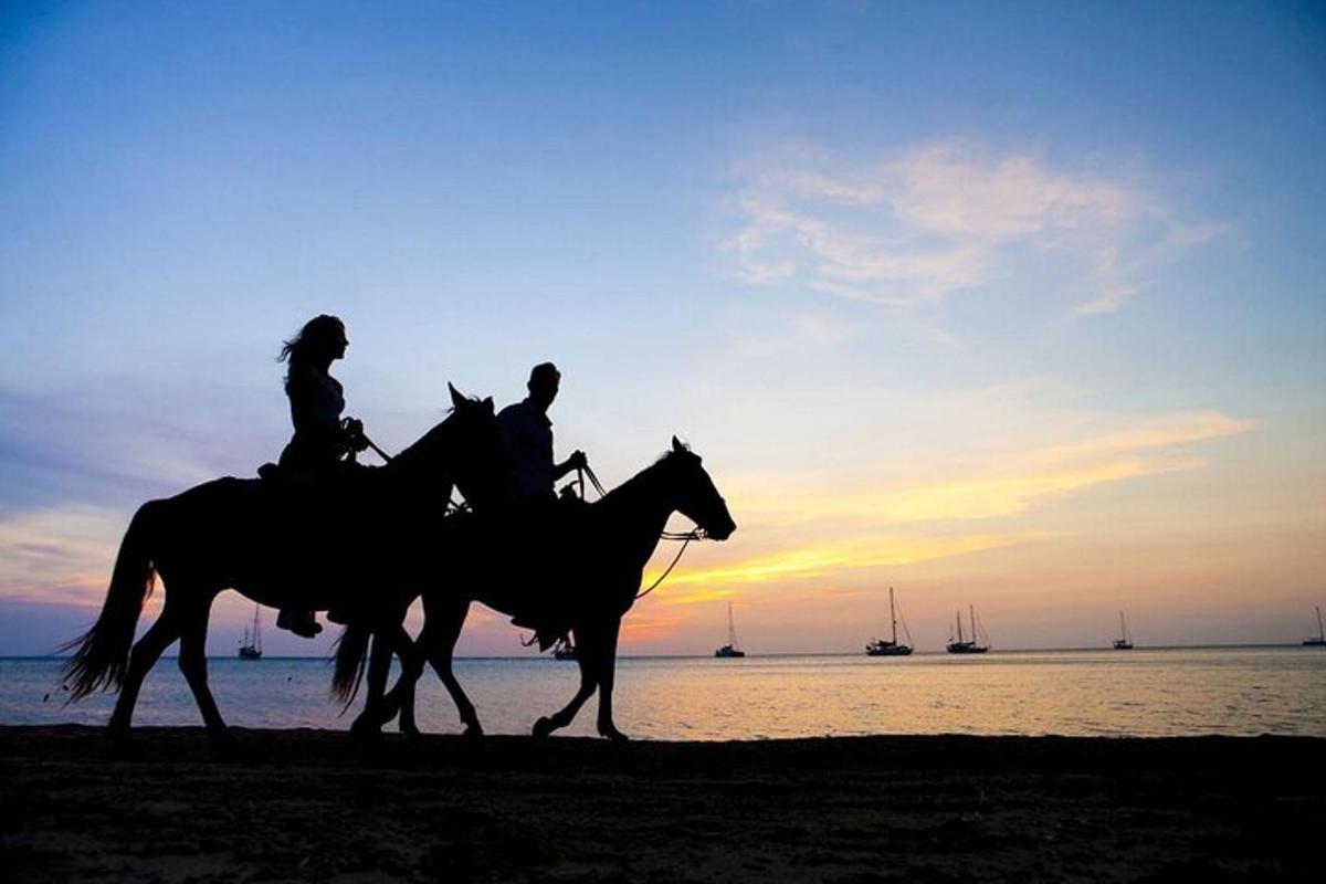 due persone a cavallo sulla spiaggia al tramonto