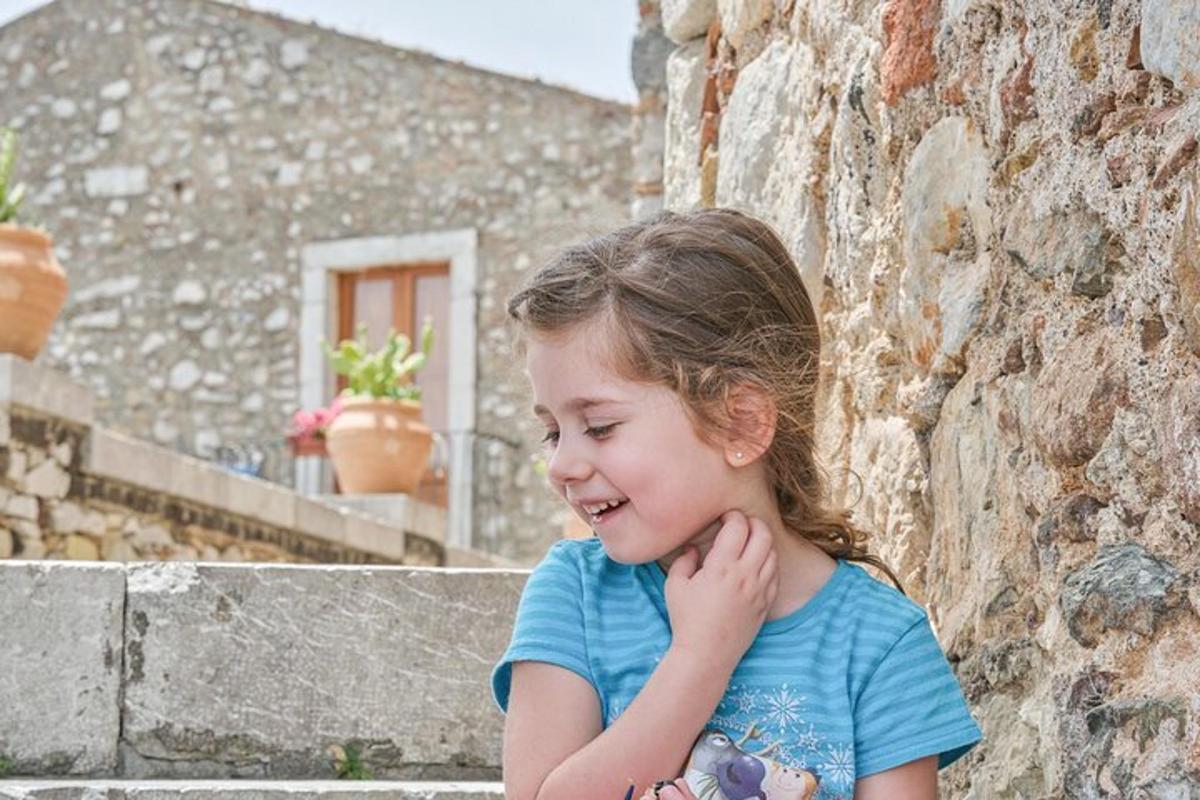 una bambina seduta accanto a un muro di pietra