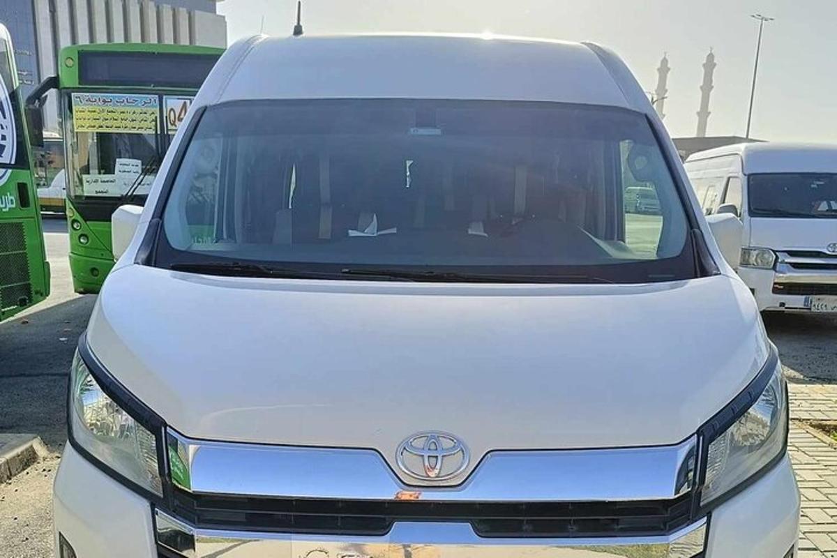 Una camioneta blanca estacionada en un estacionamiento con autobuses.