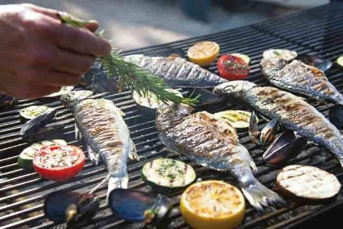 a person cooking fish and vegetables on a grill