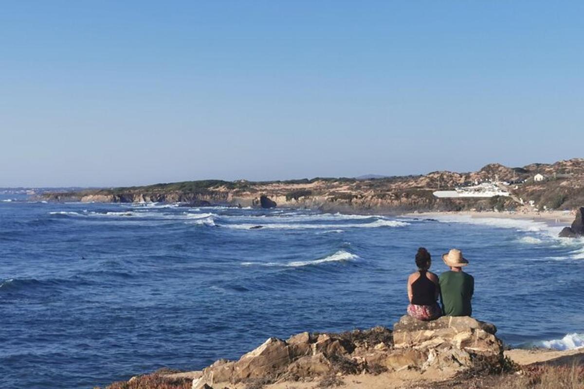 two people sitting on a rock looking at the ocean