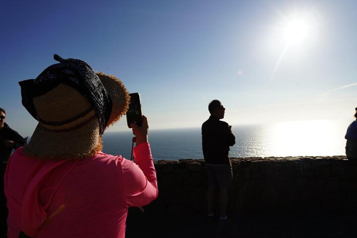a woman taking a picture of the ocean with her cell phone