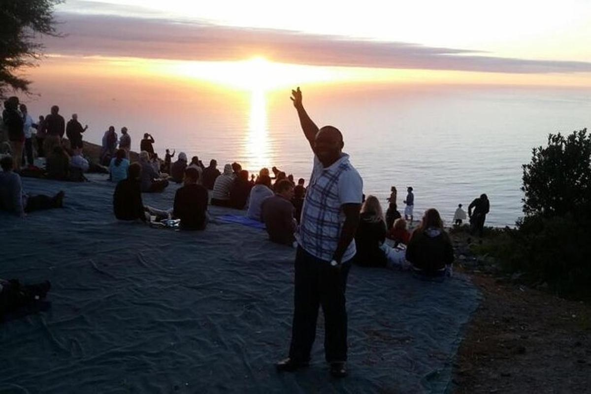 Ein Mann steht vor einer Gruppe von Menschen und beobachtet den Sonnenuntergang