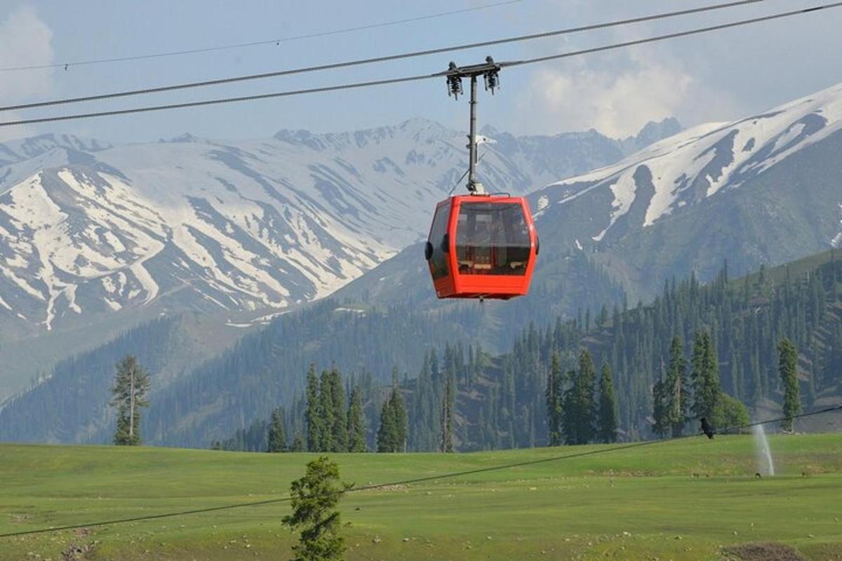 Un teleférico rojo volando sobre un campo con montañas cubiertas de nieve