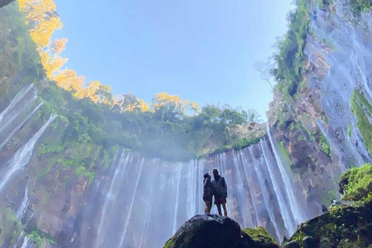 a couple standing on a rock in front of a waterfall