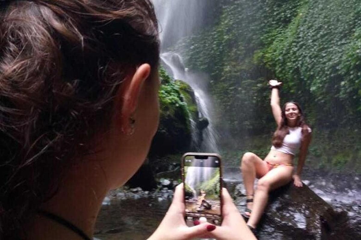 a woman taking a picture of a woman in front of a waterfall