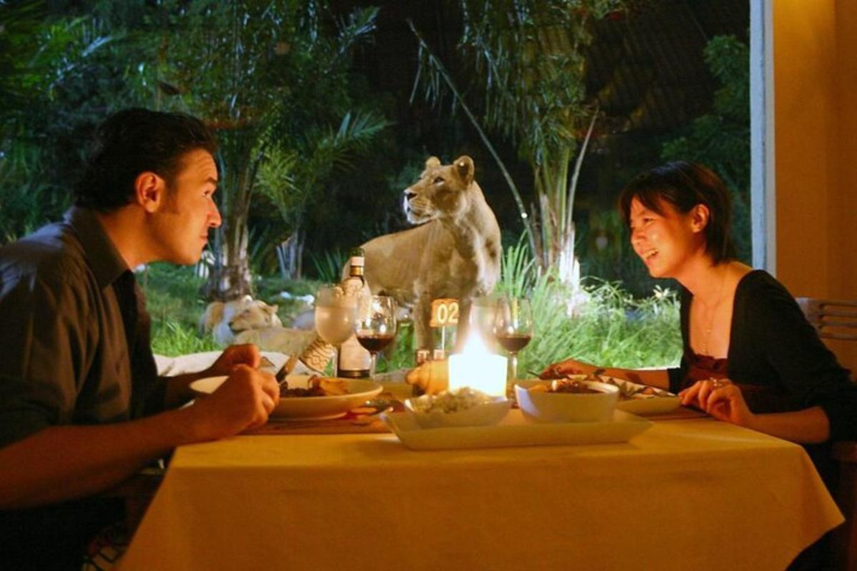 a man and woman sitting at a table with a lion in the background