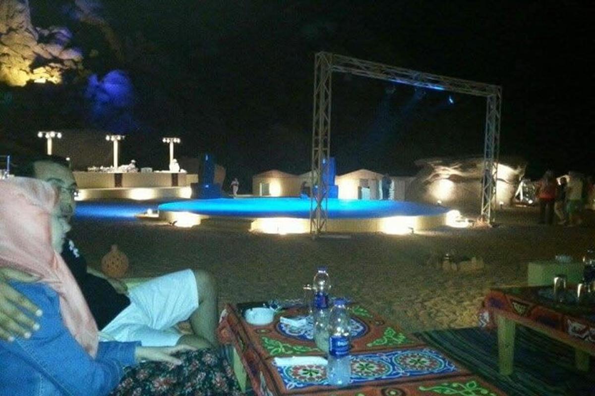 dua orang duduk di meja di hadapan kolam pada waktu malam