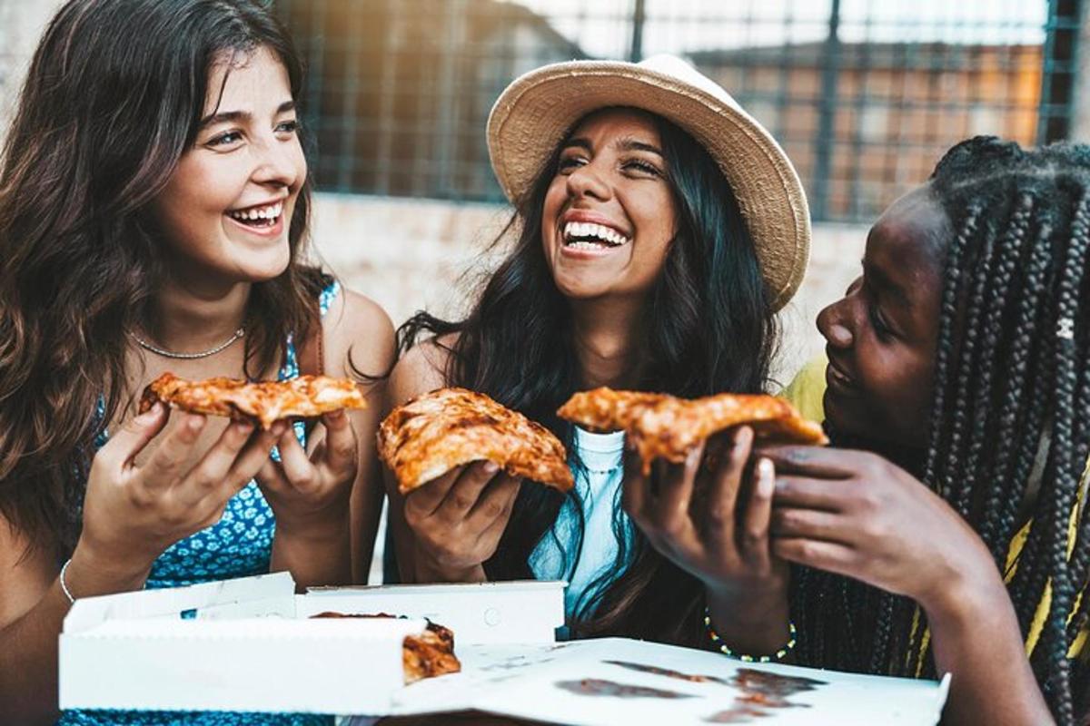 tre donne che ridono mentre mangiano fette di pizza