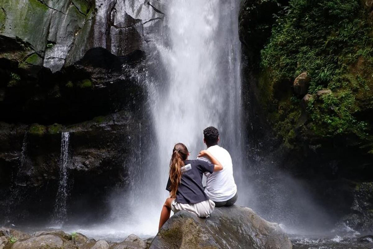 isang lalaki at babae na nakaupo sa isang bato sa harap ng isang talon