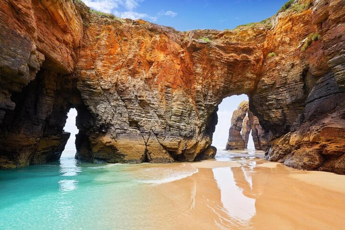 an arch in a rock wall next to a beach
