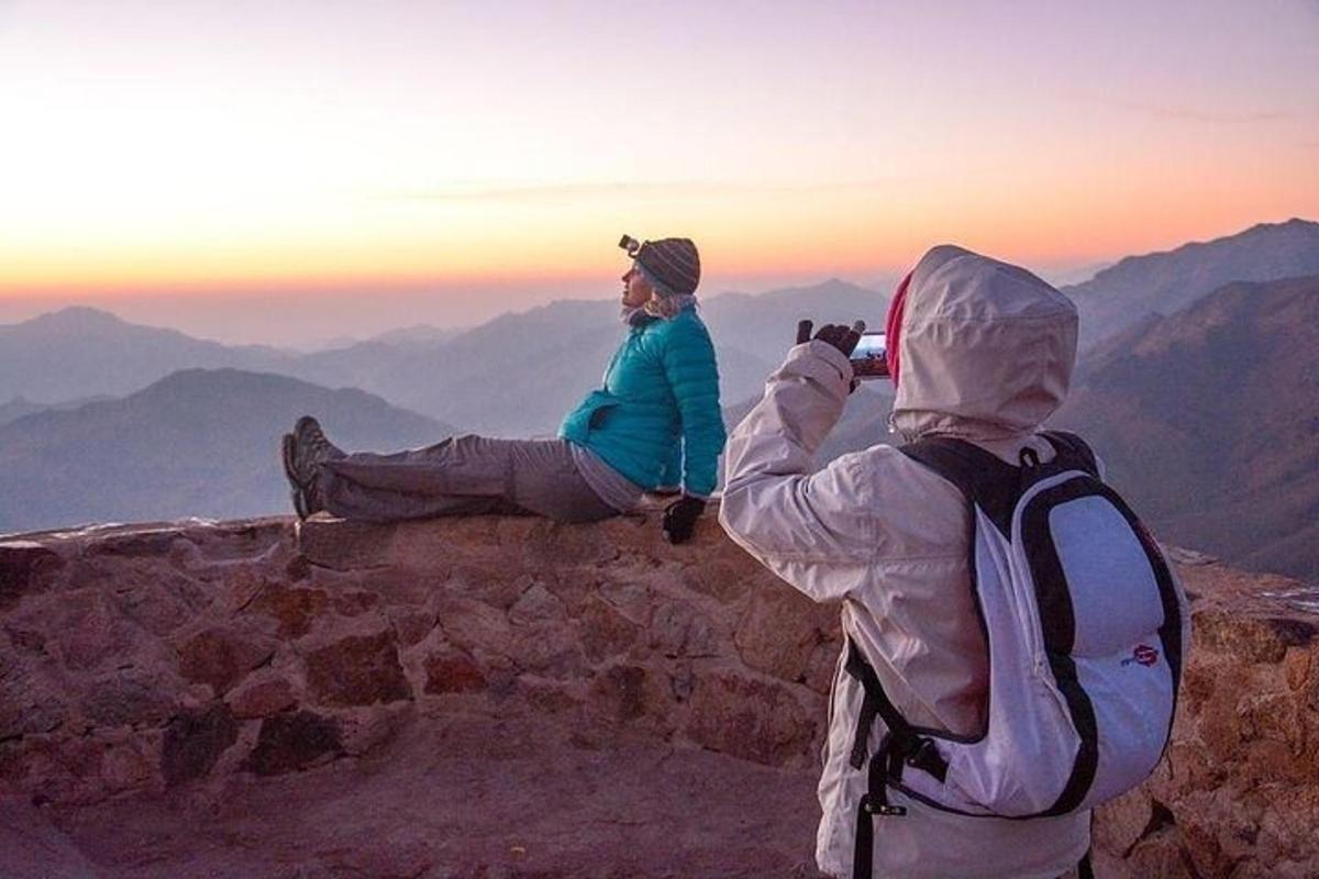 two people sitting on the edge of a mountain taking a picture