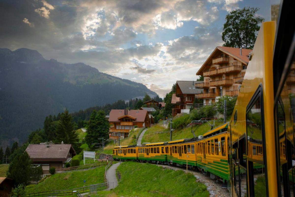 a yellow train traveling through a mountain town with houses