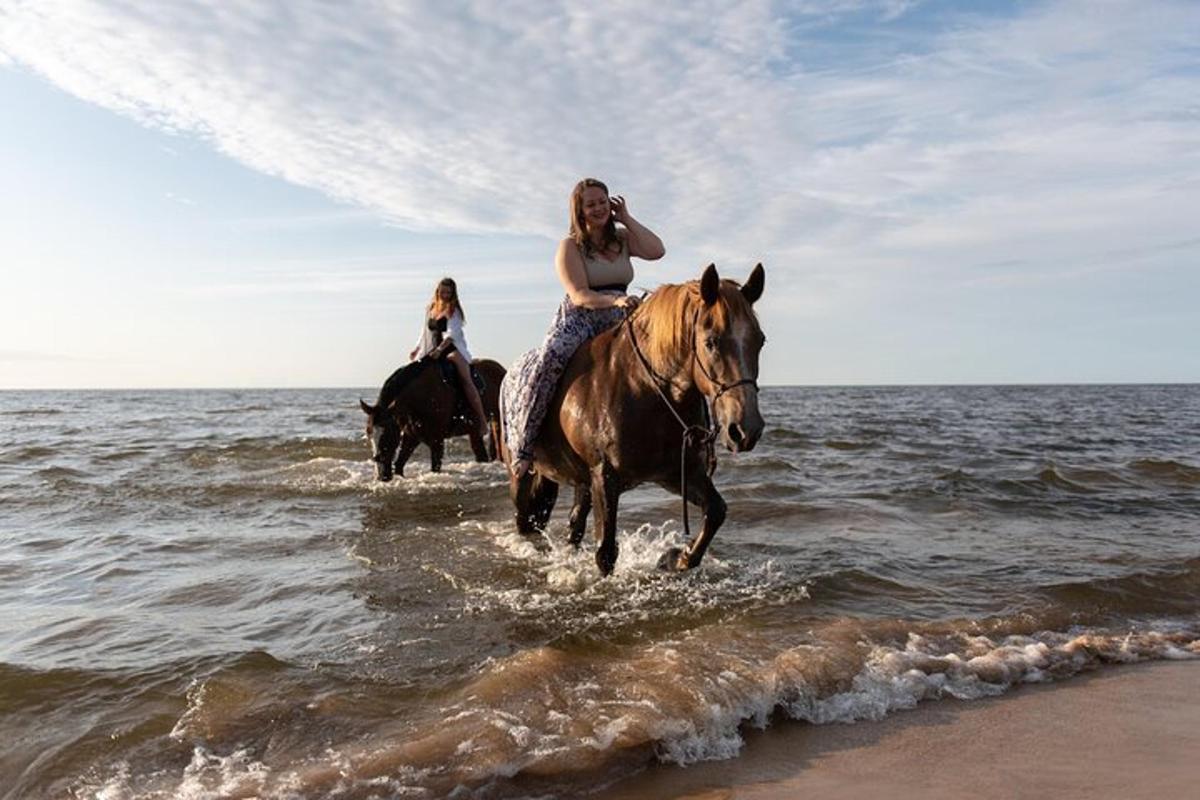 two women riding horses in the water on the beach