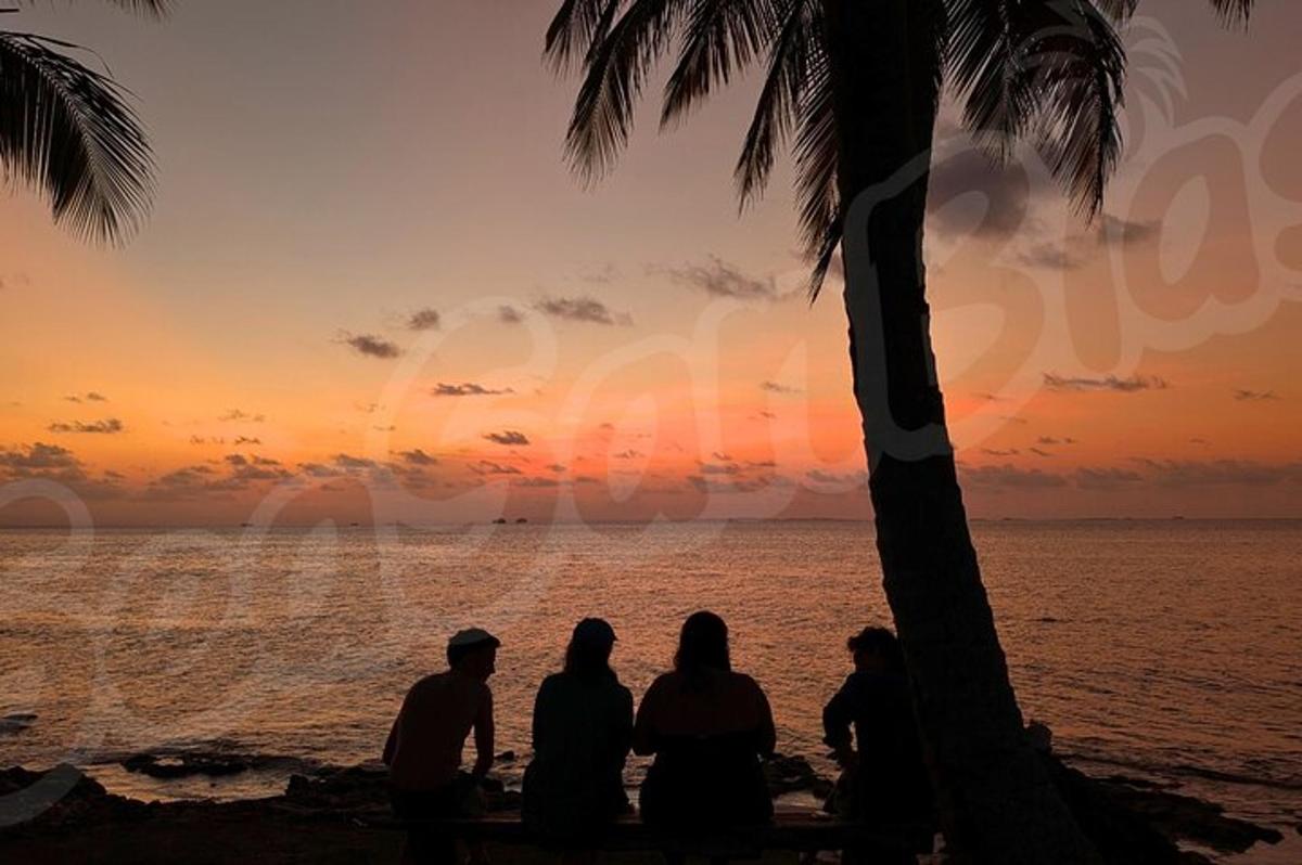 een groep mensen die op het strand zitten en naar de zonsondergang kijken