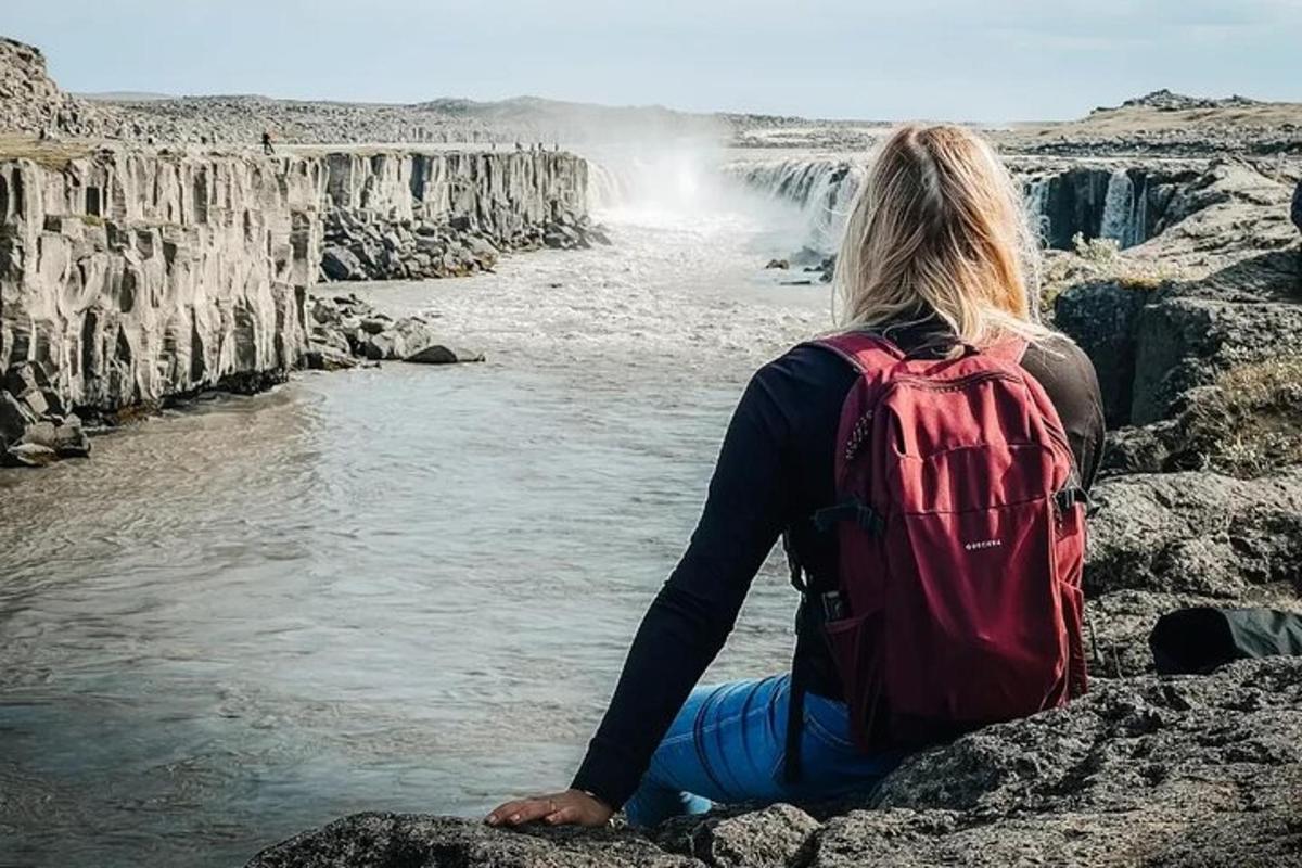 seorang wanita duduk di atas batu melihat air terjun