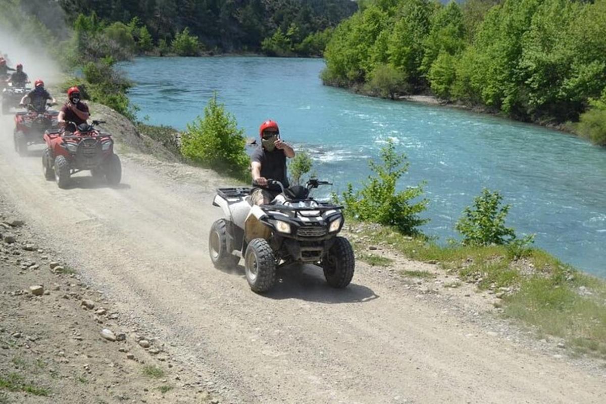 persone che guidano quad su una strada sterrata accanto a un fiume