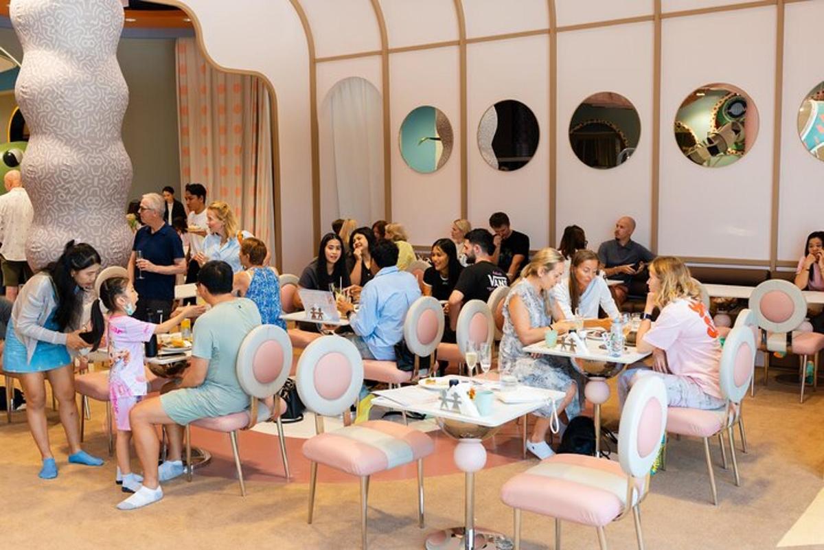cilvēku grupa, kas sēž pie galdiņiem restorānā