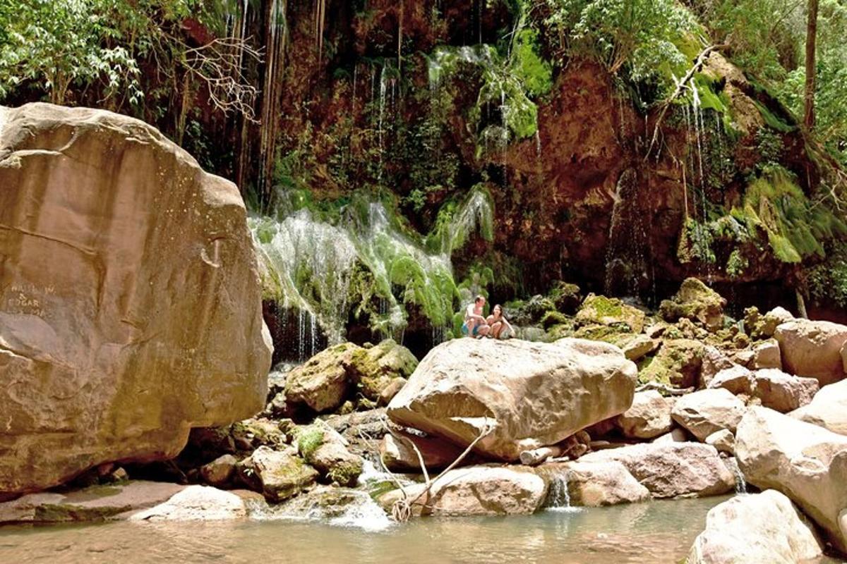 Dos personas sentadas en una pila de rocas junto a una cascada.