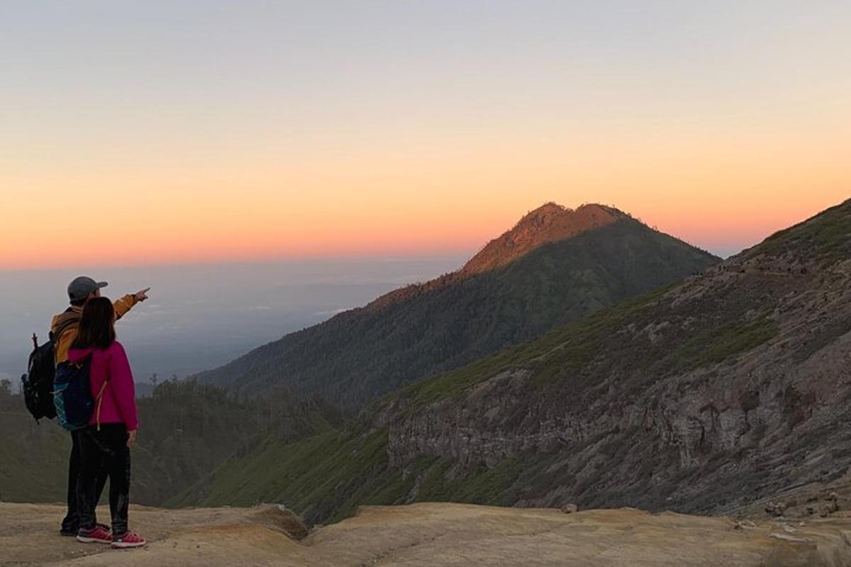 duas pessoas em pé no topo de uma montanha olhando o pôr do sol