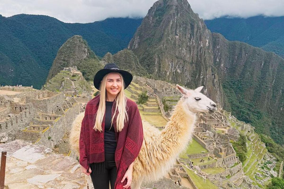 a woman standing next to a llama on a mountain