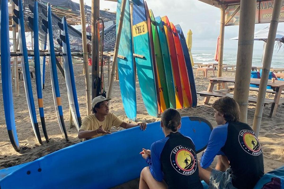 tiga orang duduk di pantai dengan papan luncur